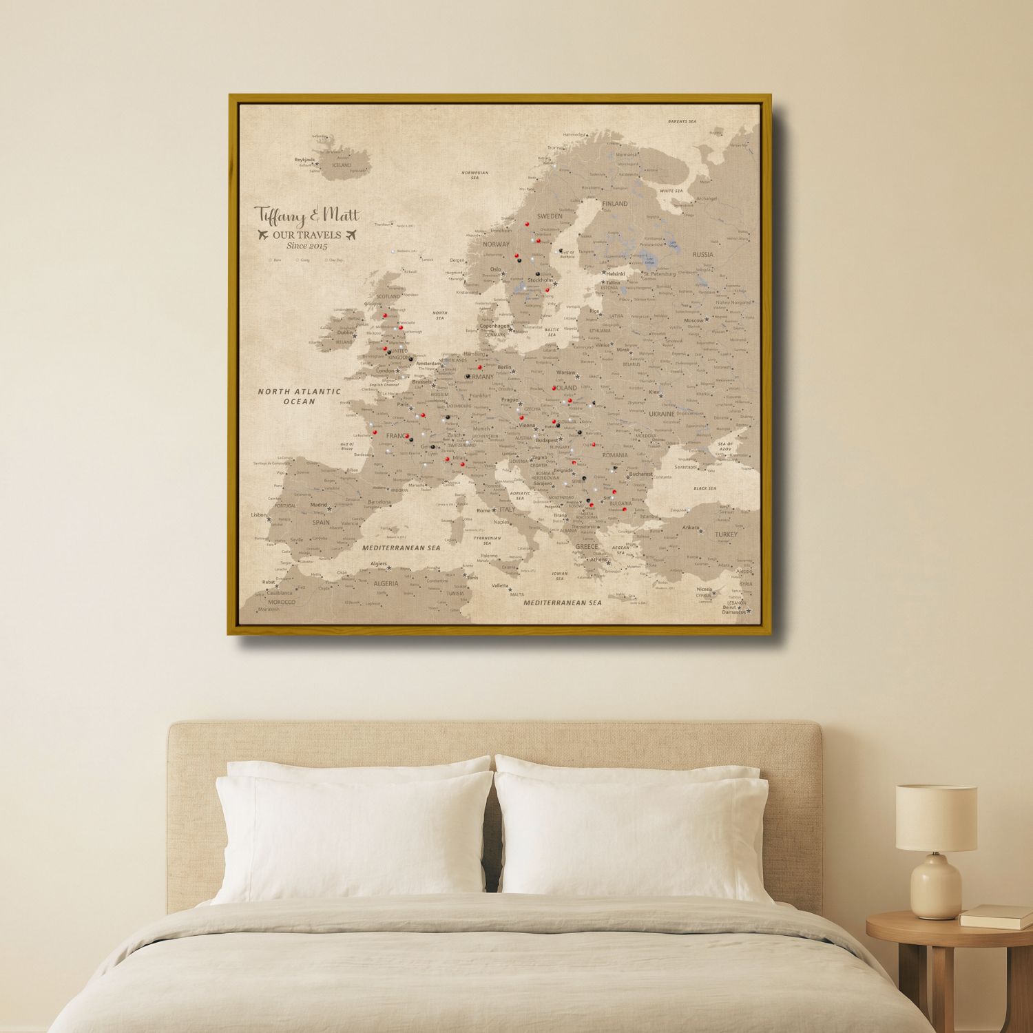 Personalized vintage Europe travel map canvas with gold frame hung above bedroom bed with pins marking destinations