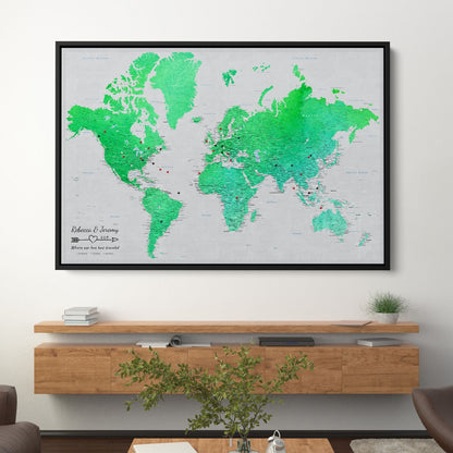 Personalized emerald green watercolor world travel map on canvas with push pins in black frame above credenza