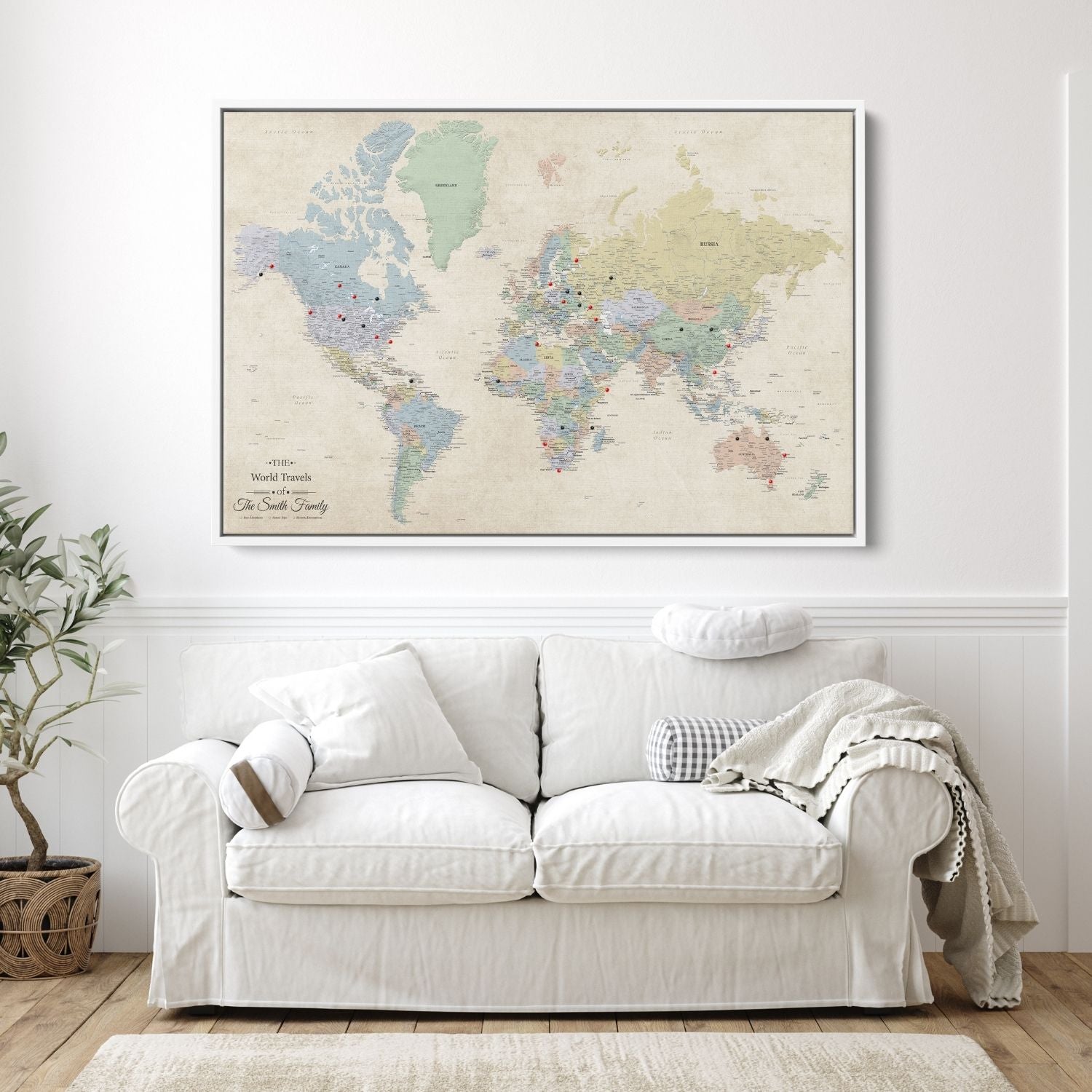 Personalized Sandy Dreams world travel map canvas in white float frame with red and black push pins hung above white sofa